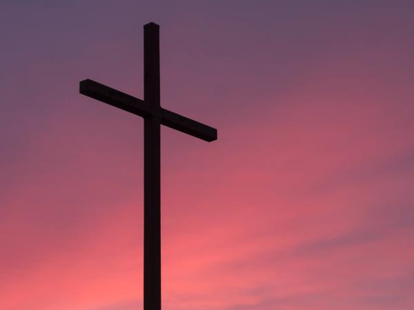 An image of a crucifix against a pink sky. Photo by Aaron Burden on Unsplash