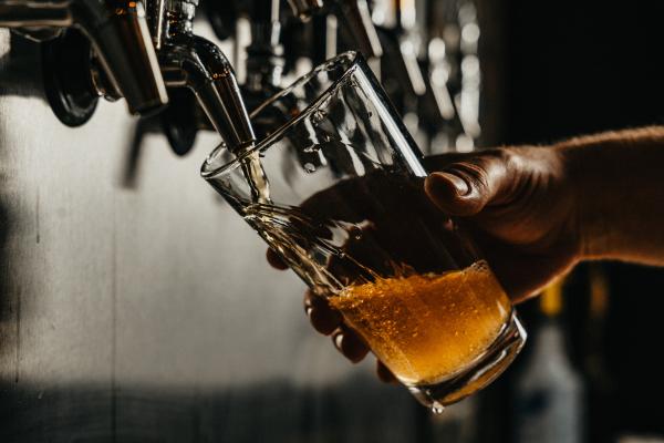 A hand holding a pint glass on an angle as an amber liquid is poured into it from a spout. Photo by Josh Olalde on Unsplash